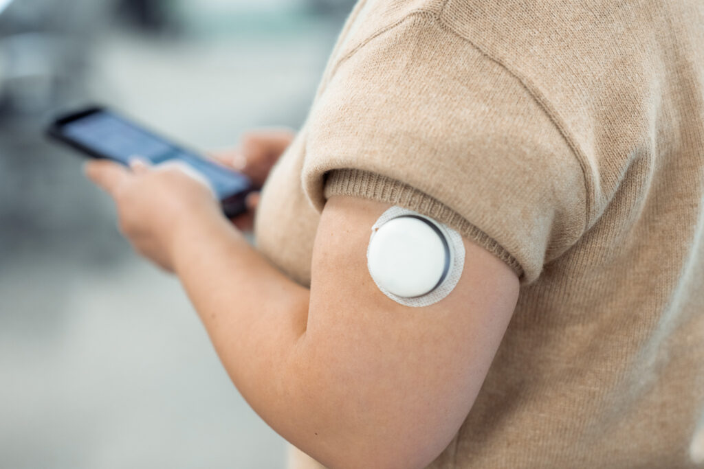 A person wearing the Pocket Clinic 7-Day Smart Injector on the upper arm while using a smartphone